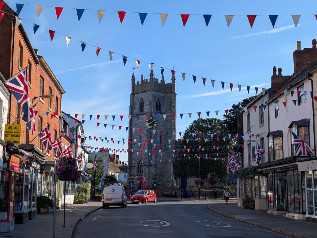 View along Alcester High Street towards St Nicholas Church, decorated with red, white and blue bunting and Union flags.